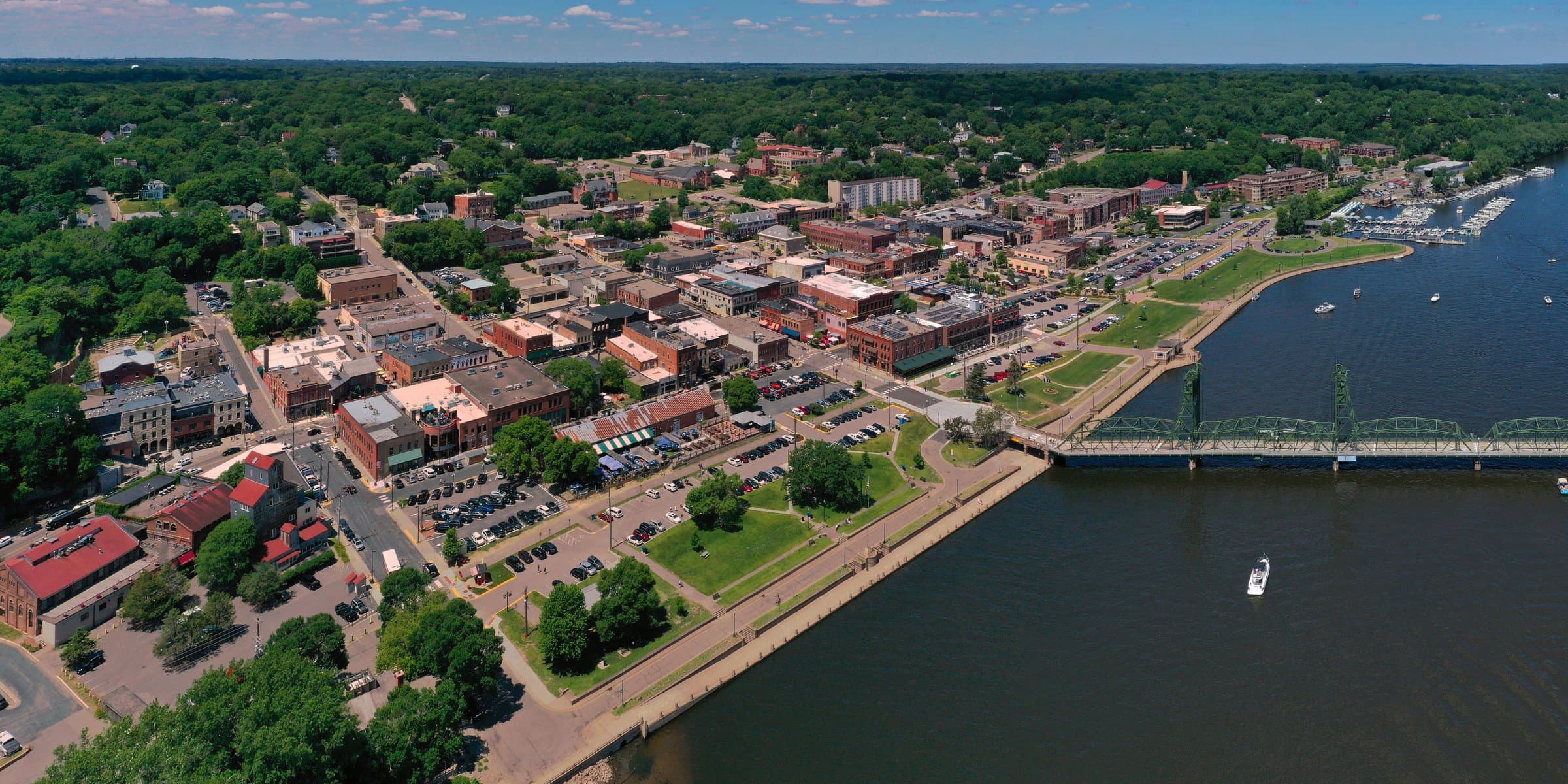 Aerial of downtown Stillwater along the St. Croix, brick storefronts above the riverfront, Lift Bridge to the right.